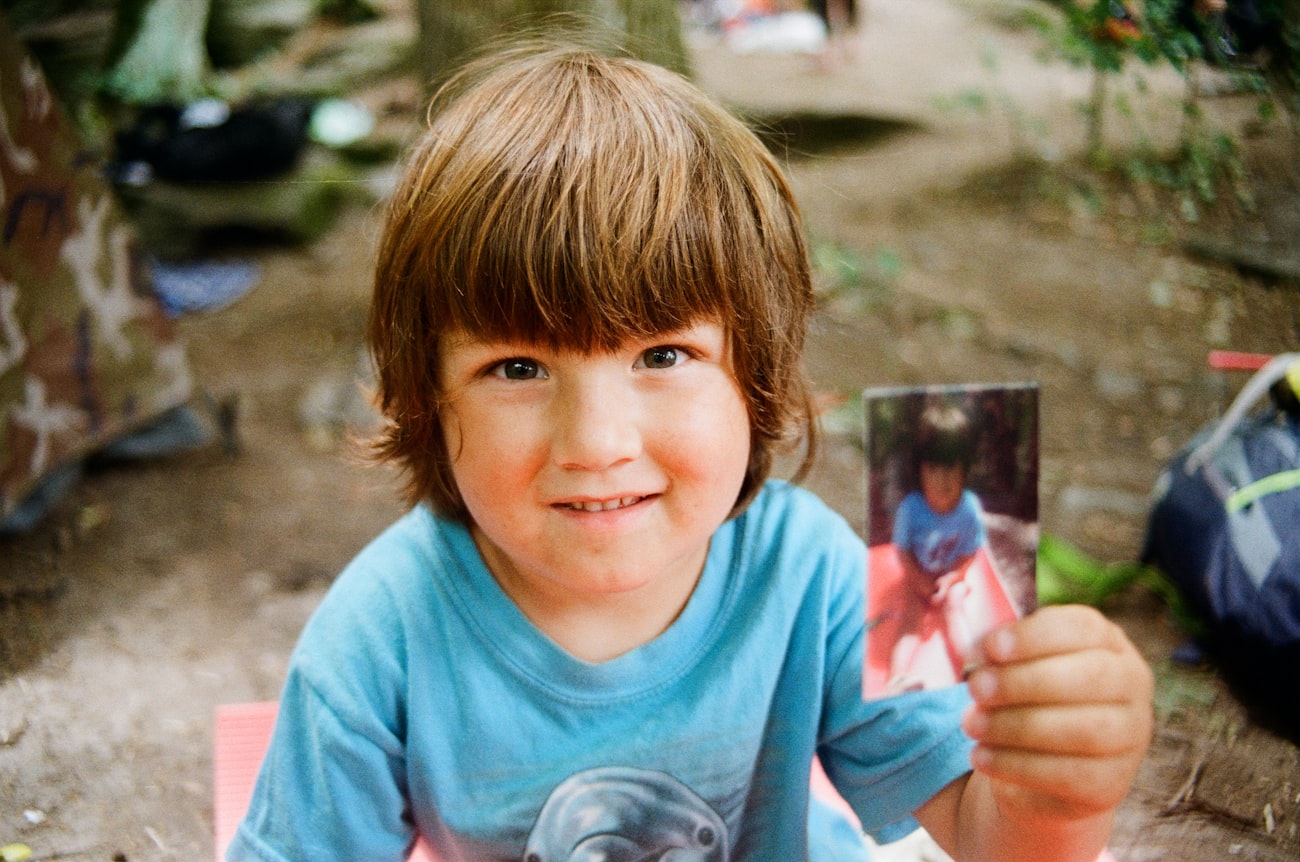 A young child smiling outdoors, holding a small photograph