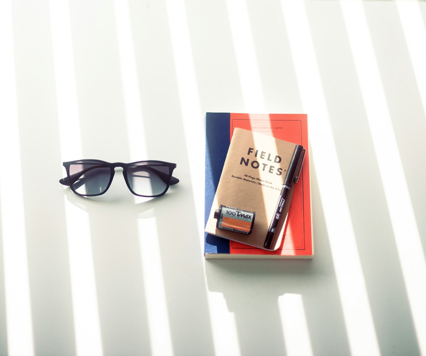 A closed notebook and pen catching light on a striped surface